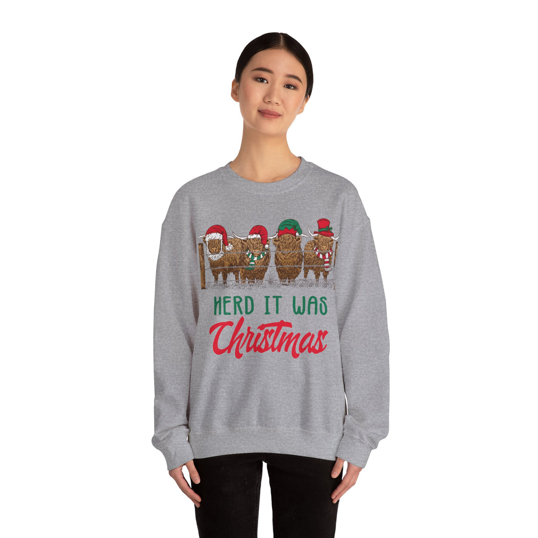 Four Highland cows lined up behind a wooden fence wearing Santa and elf hats with Herd It Was Christmas lettering in green and red, color option